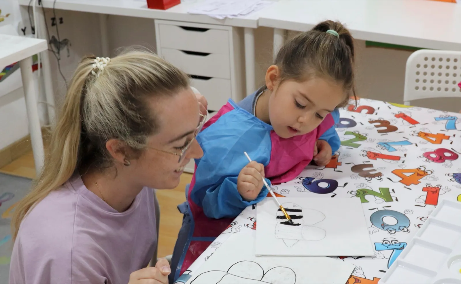 Profesora y niña pintando juntas en el aula