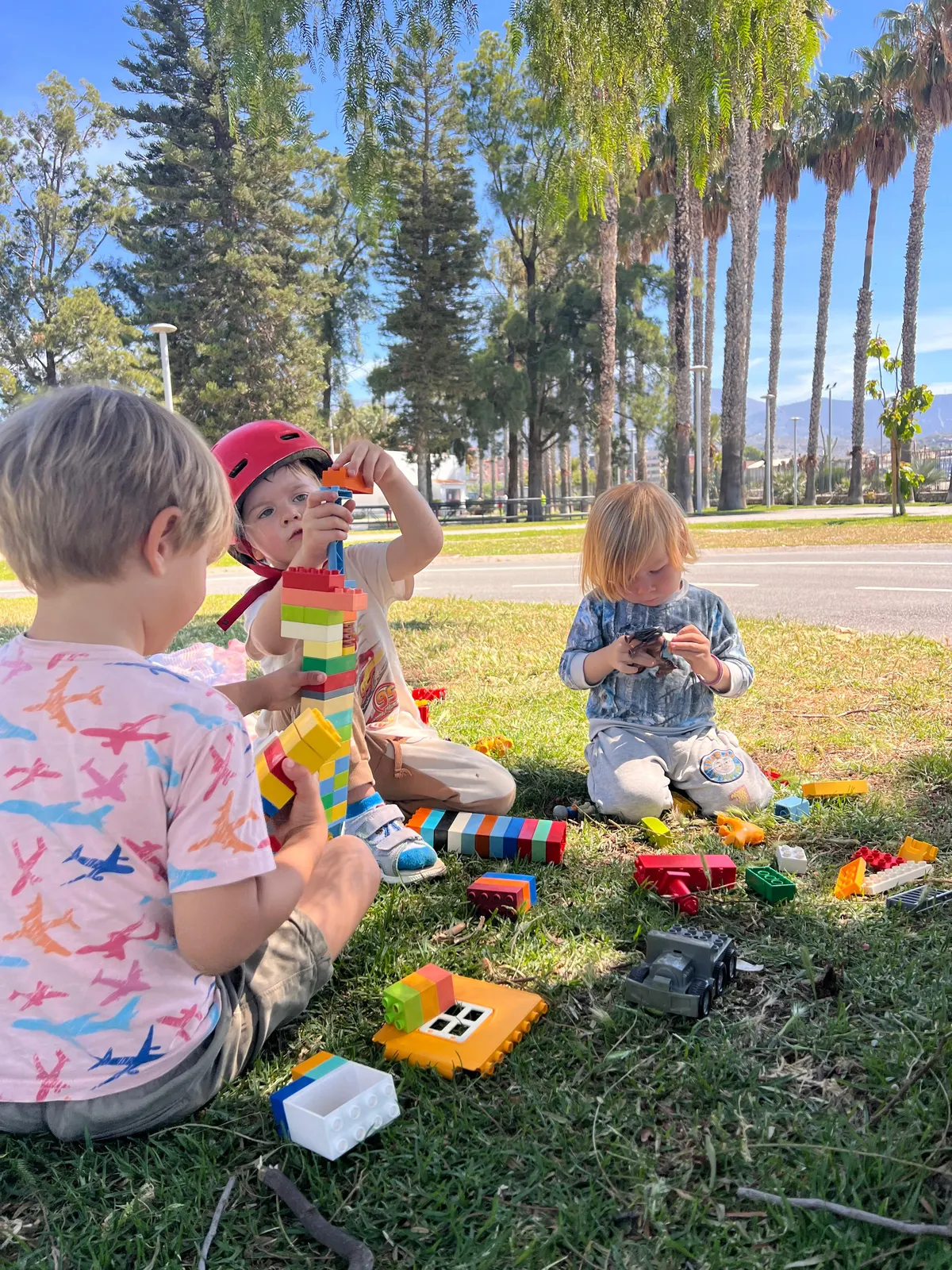 Niños construyendo con bloques de colores en la hierba bajo las palmeras