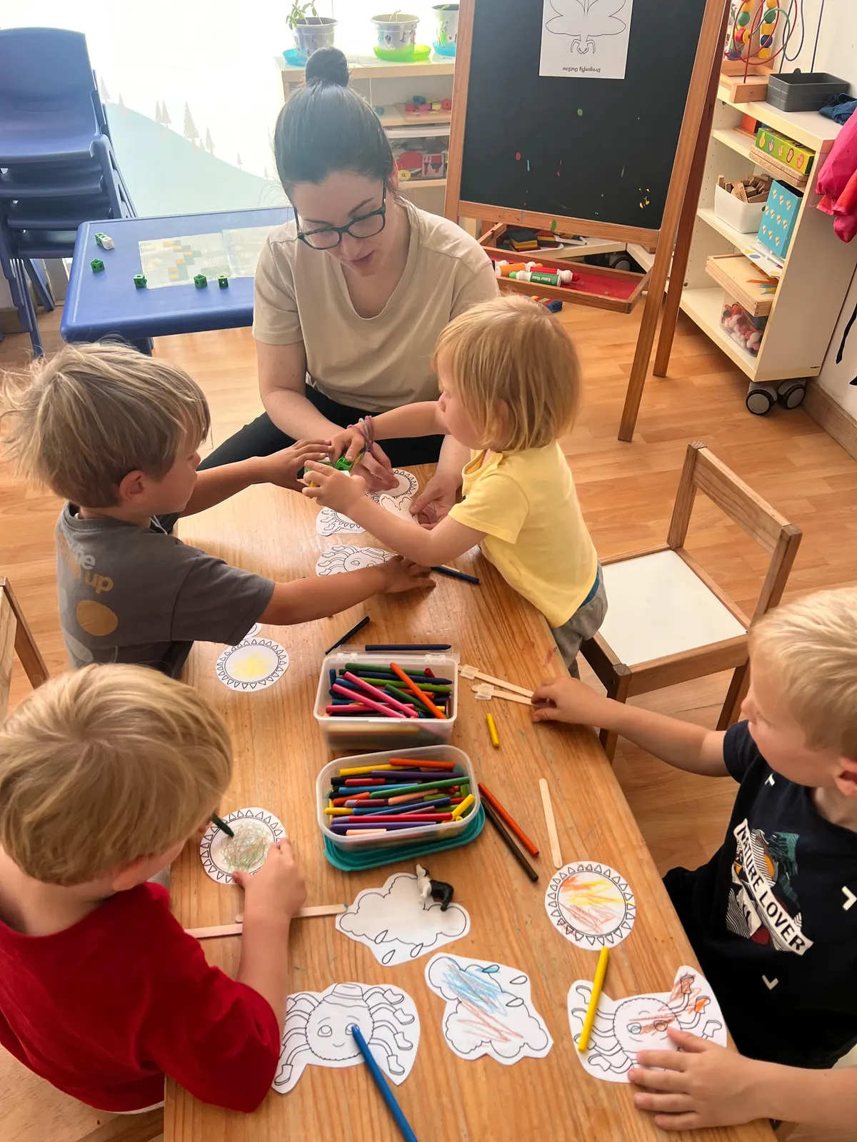Teacher helping children colour at the classroom table