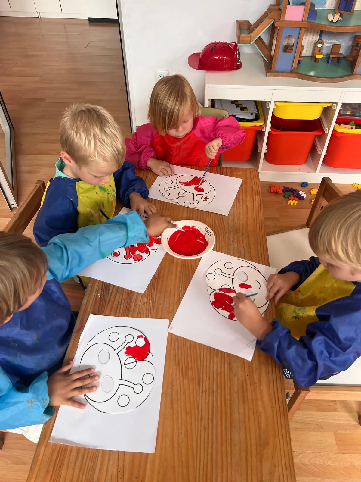 Children in smocks painting red ladybirds during art class