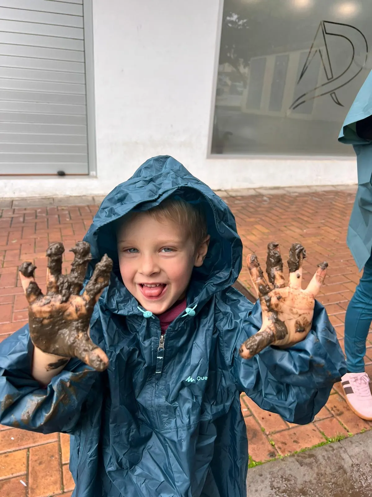 Child in a raincoat laughing and showing muddy hands after outdoor play