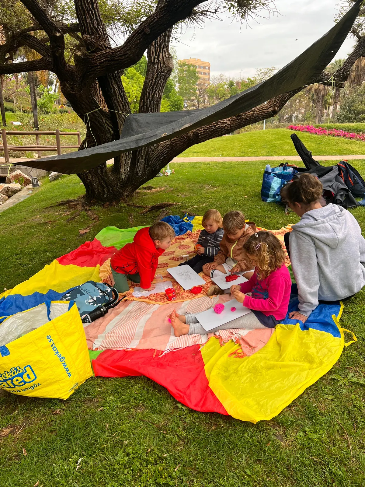Niños dibujando juntos sobre una manta paracaídas en un parque de Motril