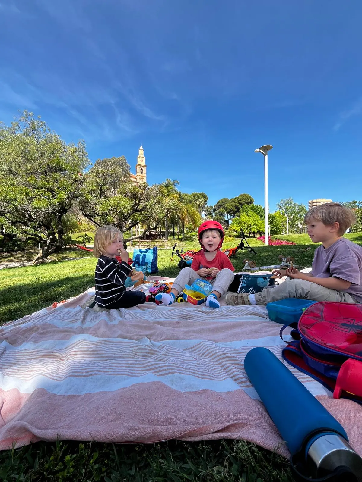 Niños en una manta de pícnic en un parque de Motril, con la torre de la iglesia al fondo