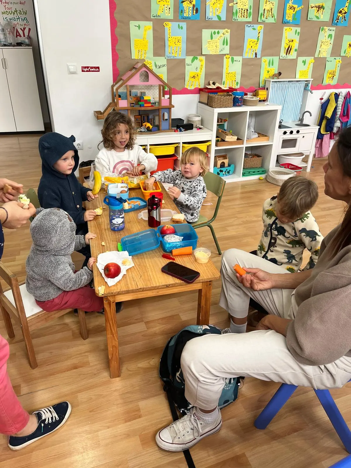 Niños compartiendo la merienda alrededor de una mesa de madera con su profesora