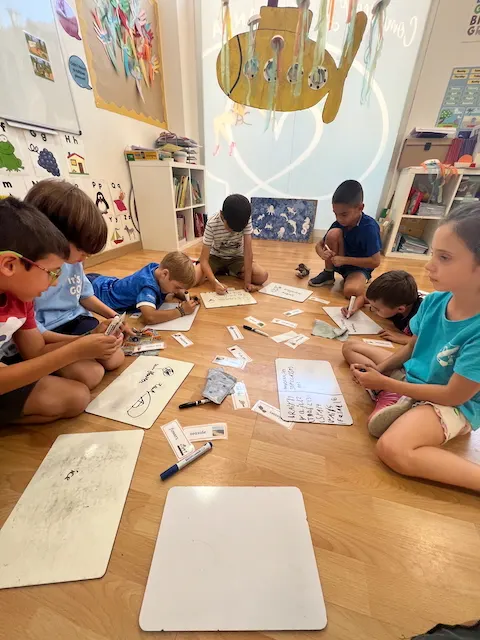 Alumnos de Ella's English en el suelo del aula trabajando con pizarras pequeñas y tarjetas de vocabulario en una sesión de phonics