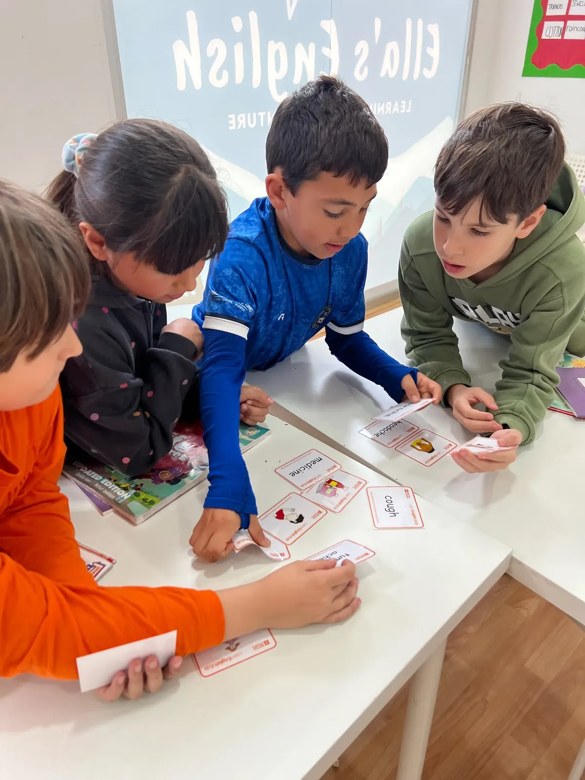 Cuatro niños clasificando tarjetas de vocabulario en inglés en una mesa blanca junto al rótulo de Ella's English