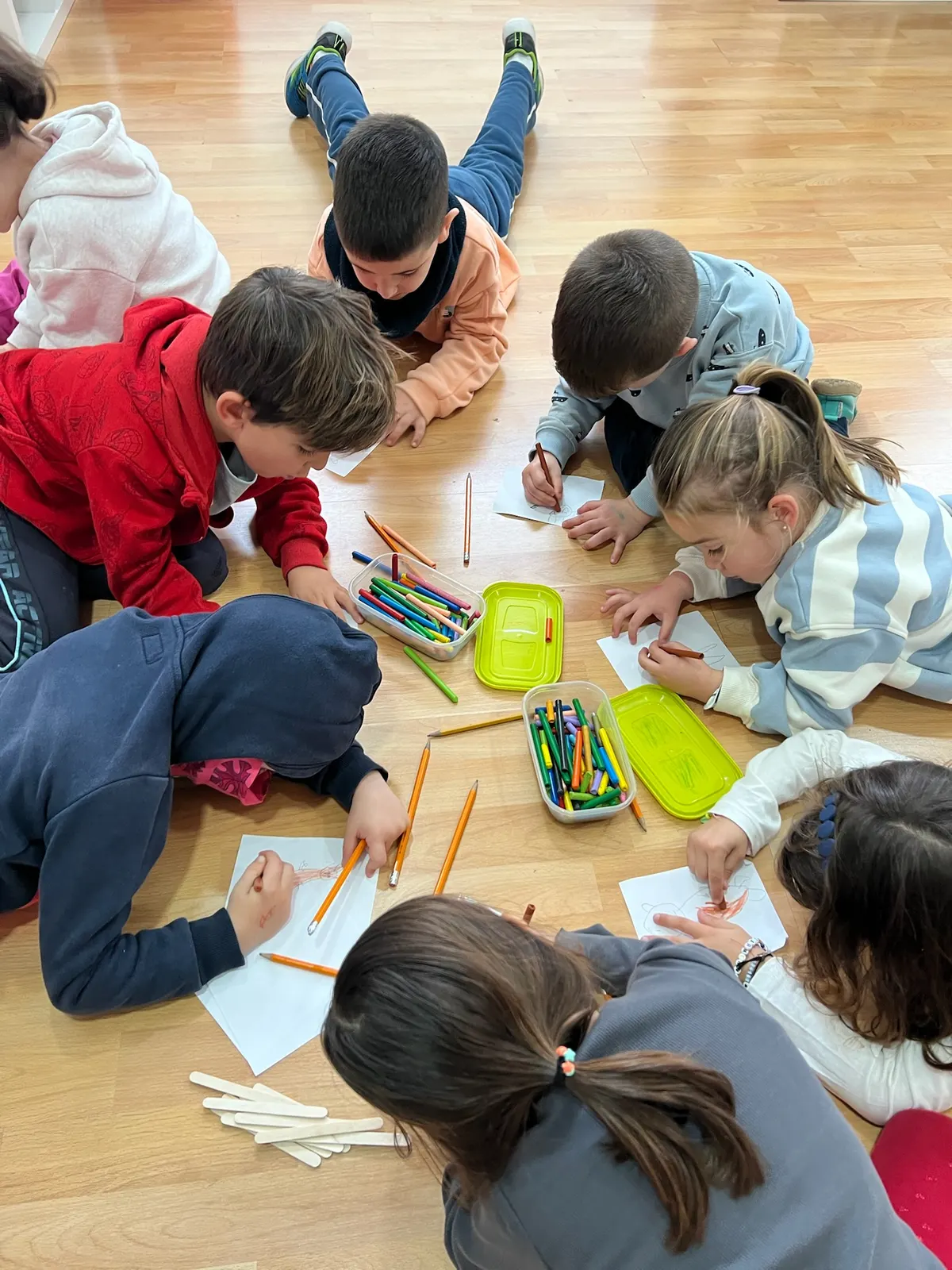Ella's English children lying on the classroom floor drawing together, sharing tubs of coloured pencils