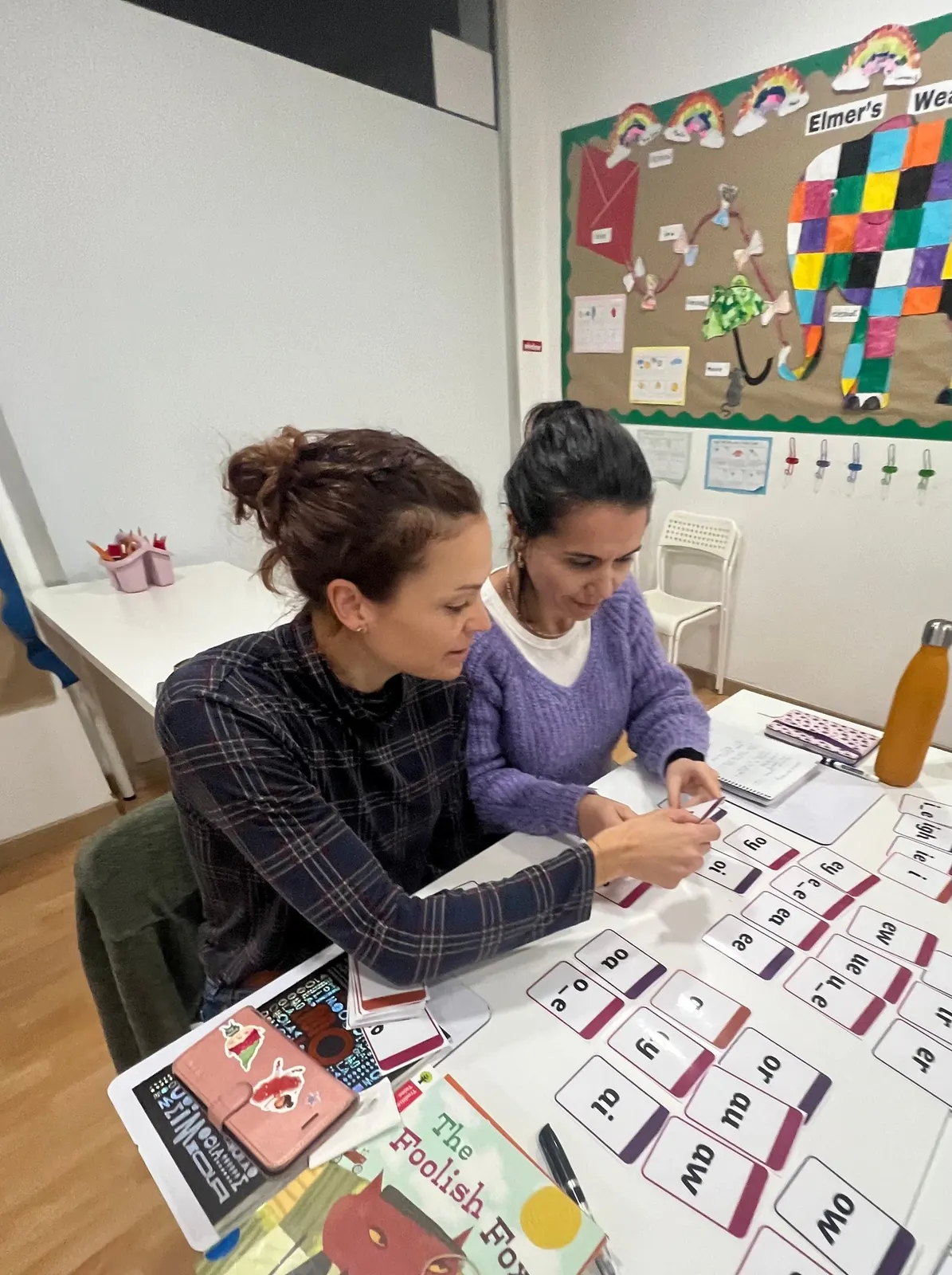 Taller Pro Phonics en marcha: profesores explorando tarjetas de sonidos, práctica de pronunciación y actividades interactivas en el aula luminosa de Ella's English.