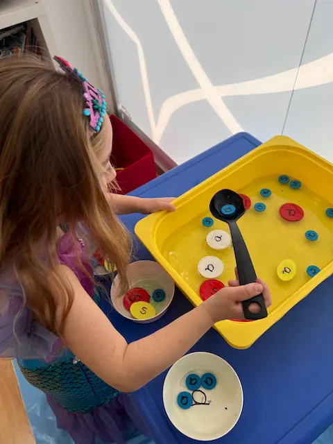 Grupo animado de profesores y familias intercambiando ideas, riendo y practicando juegos y canciones de phonics en un ambiente cálido de taller.